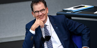 Gerd Müller sitzt im Bundestag und lacht. Eine Maske hängt ihm um den Hals.