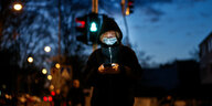 Eine Frau mit Maske im Dunkeln guckt auf ihr Handy
