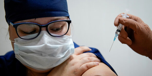 Eine Person mit Maske und Schutzanzug bekommt in einem Krankenhaus einen Impfstoff gespritzt.