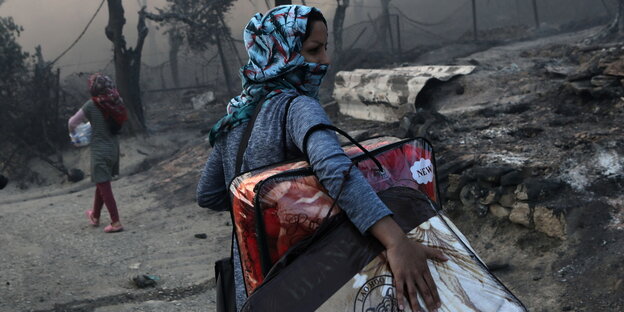 Eine Frau flüchtet mit ihren Taschen beladen aus dem brennenden Lager Moria