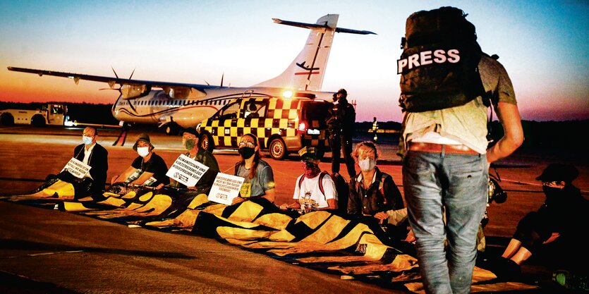 Ein Mann mit einem Rucksack mit der Aufschrift "Press" filmt Protestierende auf einem Rollfeld.