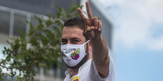 Guilherme Boulos - Bürgermeisterkandidat in São Paulo trägt Mund-Nasenbedeckung und macht das Victory Zeichen.