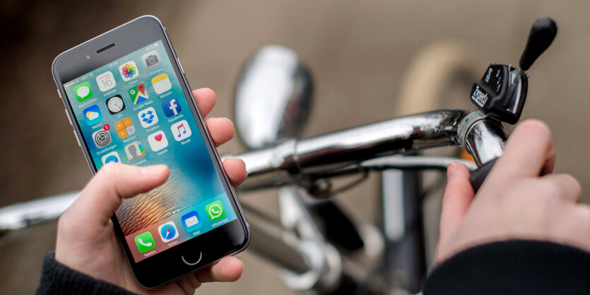 Eine junge Frau sitzt auf einem Fahrrad und bedient dabei ihr Smartphone