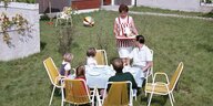 Familienszene aus den 1960er Jahren - Die Mutter serviert Tee und Gebäck im Garten für Vater und Kinder.