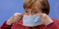 Angela Merkel setzt eine Maske auf und guckt mürrisch