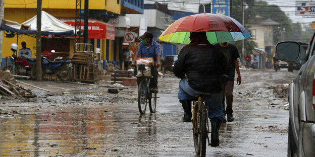 Menschen fahren auf Fahrrädern durch eine schlammige Einkaufsstraße.