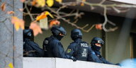 schwer bewaffnete Polizisten in Schutzausrüstung stehen auf einem Balkon, im Vordergrund verwelkte Blätter