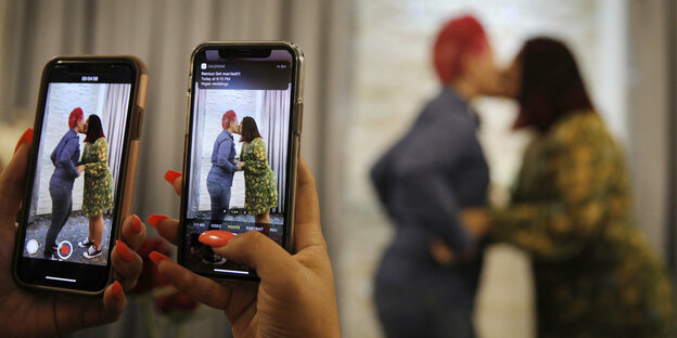 Zwei Frauen küssen sich bei einer Hochzeit in Las Vegas. Eine Dritte filmt dies mit zwei Smartphones-