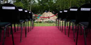 Stuhlreihen auf einem Friedhof, im Hintergrund der Aushub eines Grablochs