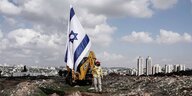 Ein Mann steht mit einer Israelfahne vor einem Bagger auf einem Baugelände
