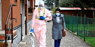 Eine Frau mit einer Mundschutzmaske hat sich bei einem Mann untergehkt, der Schutzkleidung trägt und ein Sauerstoffgerät in den Händen hält