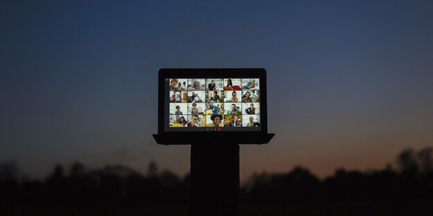 Ein Laptop auf dem eine Videokonferenz mit mehreren teilnehmern zu sehen ist steht während eines Sonnenuntergangs draußen auf einem Podest.