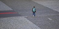 Ein Schüler mit einem Ranzen auf dem Rücken geht von der Betrachter:in weg