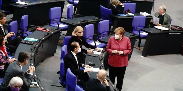 Angela Merkel trägt einen Mundschutz und spricht mit Abgeordneten