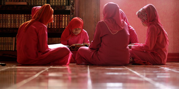 junge Frauen in pinken Gewändern sitzen im Schneidersitz in einer Moschee und lesen Verse im Koran