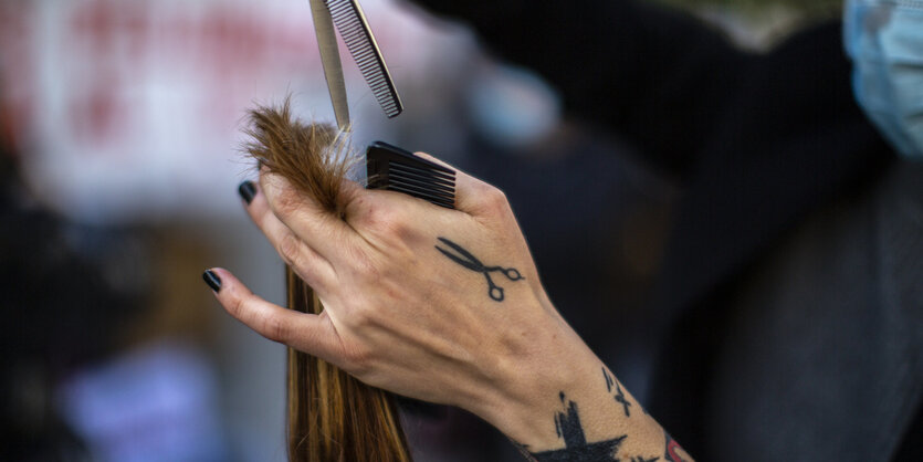 Eine Friseurin schneidet einer Frau die Haare. Auf ihrer Hand ist eine Schere tättowiert.