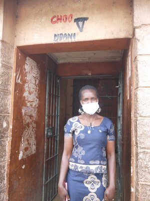 Eine Frau mit Mundschutz steht vor einem Eingang.