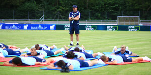 Spieler der TSG Hoffenheim liegen auf Yogamatten auf dem Rasenplatz. Vor ihnen steht ein Trainer