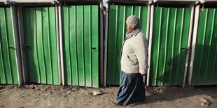 eine schwarze Frau geht an einer Reihe von öffentlichen Toiletten mit grüner Tür, vorbei