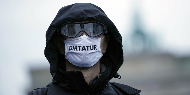 Demonstrant verhüllt mit Kapuze, dunkler Brille und einer Gesichtsmaske mit der Aufschirft: Diktatur