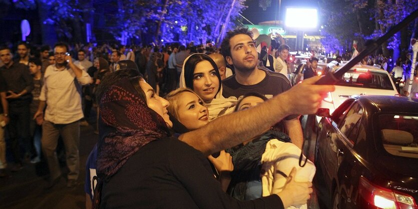 Menschen machen ein SElfie vor einer Menschenmenge auf einer nächtlichen Straße in Teheran