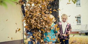 drei kleinere Kinder werfen Laub in idie Luft