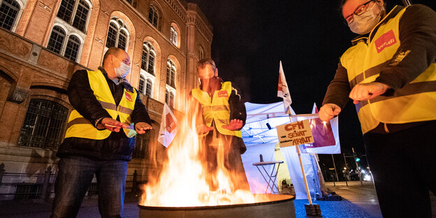 Drei Männer wärmen nachts ihre Hände an einer Feuertonne, die sie vor dem Roten Rathaus aufgestellt haben