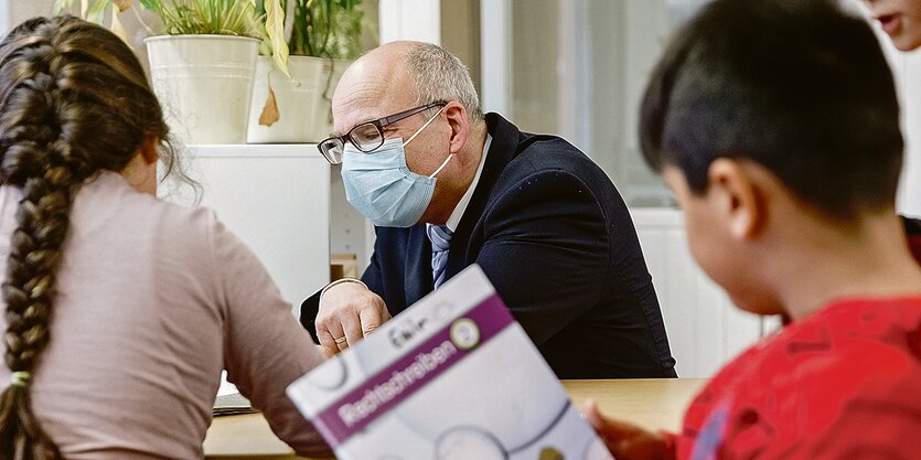 Zwei Kinder und ein Mann mit Mundschutz sitzen am Tisch