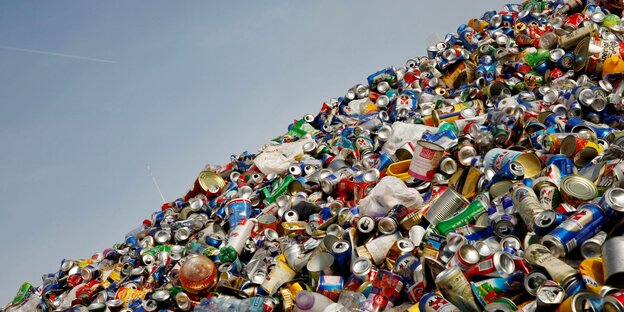 Eine Sammelstelle für Recycling - Viele Aludosen und andere Verpackungsmaterialien liegen vor blauem Himmel auf einem haufen.