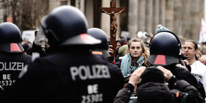 Eine junge Frau mit Holzkreuz an dem Jesus hängt steht in der Menge vor der Polizeirehe