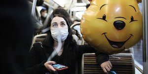 eine junge Frau sitzt mit Smiley-Luftballon in der U-Bahn