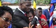 Bobi Wine hält eine Frau im Arm und streicht ihr übers Haar, umringt von UnterstützerInnen mit Fahnen