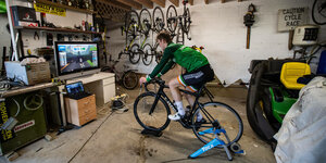 Ein Radprofi fährt auf einer Rolle im Keller vor einem Bildschirm ein Rennen