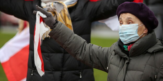 Eine Frau in höherem alter hält eine belarussische Flagge in der Hand.