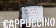 Hinter Glasscheibe, auf der Cappuccino geschrieben ist,steht ein Schild "Wegen Corona geschlossen"