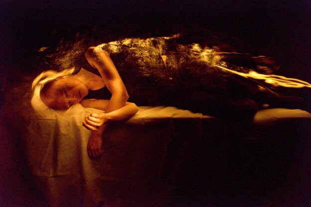 Eine Frau liegt auf einem Podest, den Körper von Licht umrahmt.