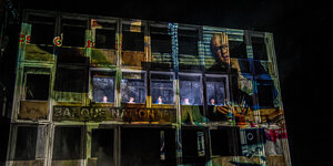 Menschen schauen aus einem bunt angeleuchteten Haus; Szene aus dem Stück "Dantons Tod"