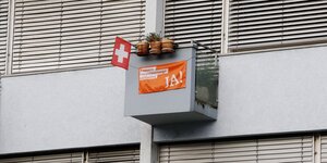 Ein kleiner Balkon ist mit Blumentöpfen, Schweizer Fahne und Banner der Konzernverantwortungsinitiative bestückt.