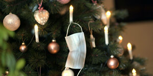 Eine Mund-Nasenschutz-Maske hängt an einem geschmückten Weihnachtsbaum.