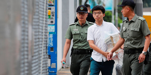 Joshua Wong, ein junger Mann in weißem Kurzarmhemd wird von zwei Polizisten geführt.