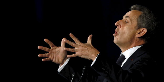 Frankreichs ehemaligem Staatspräsidenten Nicolas Sarkozy gestikuliert vor schwarzem Hintergrund-