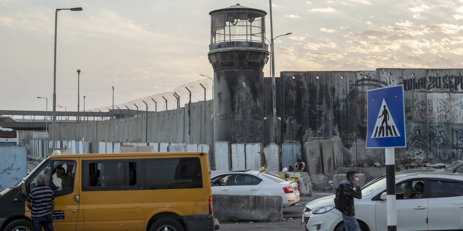 Strassenszene in Qalandia: Grenzmauer von Israel mit Wachturm und ein gelbes Taxi