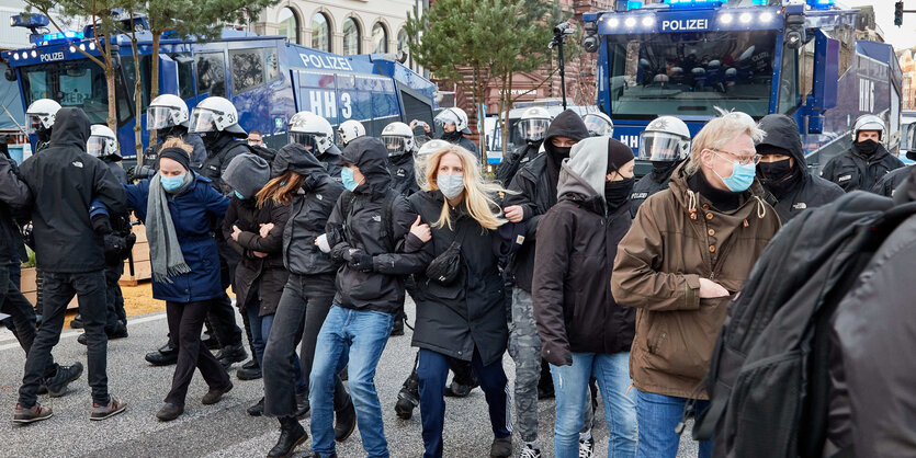 Demonstranten bilden eine Kette, hinter ihnen Polizisten und Wasserwerfer