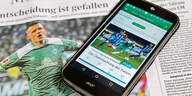 Ein Smartphone mit der Werder-App liegt auf einer Zeitungsseite des Weser-Kuriers.