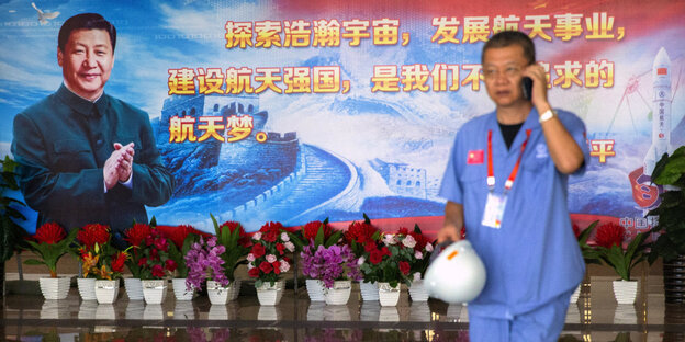 Ein telefonierender Mann vor einer Palkatwand, die Xi Jinping zeigt