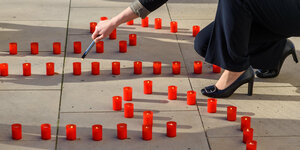 Eine Politikerin des Landtages von Sachsen-Anhalt zündet vor einer Gedenkveranstaltung anlässlich des "Tages gegen Gewalt an Frauen" vor dem Landtag Kerzen an, die zusammen die Zahl "117" darstellen.