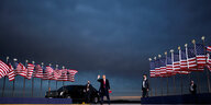 Donald Trump an einem Flughafen in Iowa winkt und hält eine Make America Great Again Mütze in der Hand.