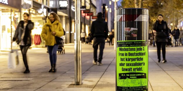 Frauen flanieren über die winterliche Fußgängerzone von Stuttgart. Im Vordergrund ein Plakat, das Gewalt gegen Frauen problematisiert