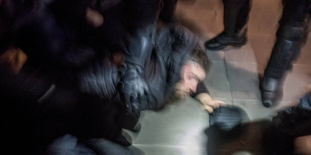 Ein Mann liegt auf dem Boden. Ein Polizist und weitere Personen stehen daneben.