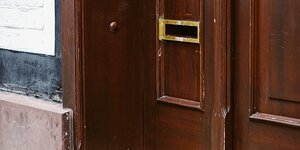 Ein Briefkastenschlitz ohne Klappe in einer Tür aus Holz.